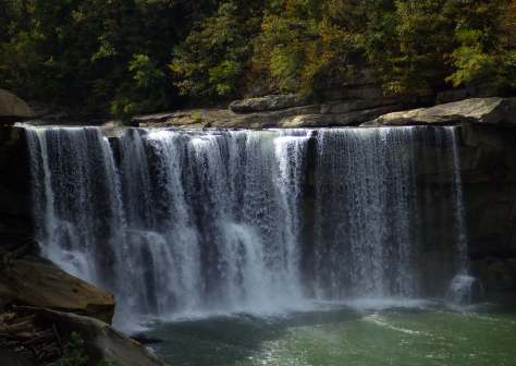 A scenic waterfall cascading down rocky cliffs into a serene pool, surrounded by lush green trees and autumn foliage.